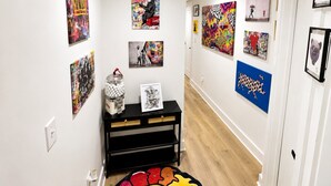 Un couloir orné d’œuvres d’art aux murs, une console noire et un tapis aux couleurs vives.