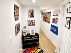Een gang met kunst aan de wanden, een zwarte consoles en een kleurrijk vloerkleed.