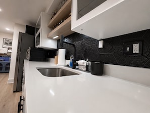 Eine moderne Küche mit weißer Arbeitsplatte, Spüle aus Edelstahl und schwarzem Fliesenspiegel.