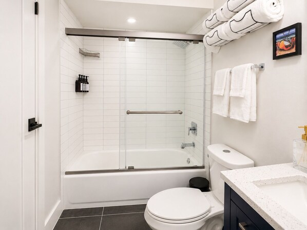Une salle de bain moderne avec une douche à parois de verre, des toilettes blanches et un lavabo doté d’un plan de travail à motifs.