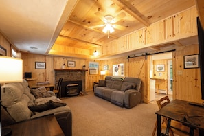A cozy cabin interior with a fireplace, wooden walls, a ceiling fan, and a dining area. - Ligonier Relaxing Country 2 Bedroom Ranch – Fallen Oak,  
Sauna, Cold Plunge, MC (Ligonier)
