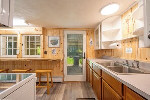 A kitchen with wooden cabinets, a sink, and a glass door leading outside. - Ligonier Relaxing Country 2 Bedroom Ranch – Fallen Oak,  
Sauna, Cold Plunge, MC (Ligonier)