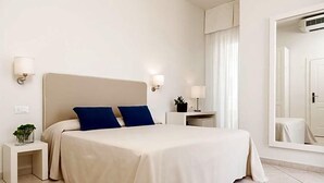 A hotel room with a bed, bedside tables, a mirror, and a wall-mounted air conditioning unit. - Hotel Capanni (Bellaria-Igea Marina)