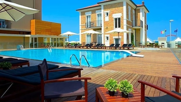 A swimming pool with lounge chairs and umbrellas, surrounded by a wooden deck and a building with balconies. - Hotel Capanni (Bellaria-Igea Marina)
