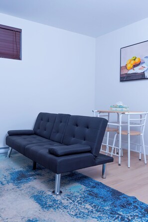 Ein modernes Wohnzimmer mit einem dunkelgrauen Sofa, einem kleinen runden Tisch und einem blauen Teppich mit Muster.