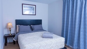A neatly made bed with a headboard, a bedside lamp, and a framed picture on the wall. - Honeycomb Suite, 2 minutes to MillCreek nature park (Riverview)