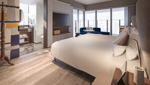 Quarto de hotel moderno com uma cama grande, televisão, sofá e vista para a cidade.