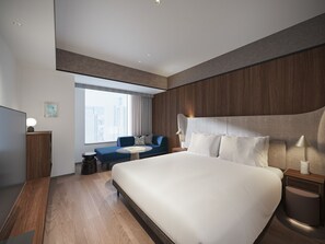 Quarto de hotel moderno com uma cama grande, um sofá, uma mesa de escritório e vista para a cidade.