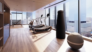 Uma academia moderna com equipamentos de exercício, um saco de pancada preto grande e vista para a cidade através de amplas janelas.