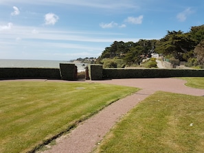 A coastal pathway with a gate, grassy areas, and a view of the sea and buildings in the distance. - Ground-floor apartment facing the sea with a large terrace (Pornic)