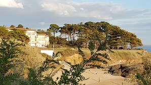 A coastal landscape with a building, trees, and a sandy area. - Ground-floor apartment facing the sea with a large terrace (Pornic)