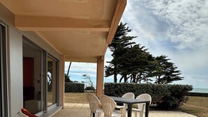 A covered outdoor seating area with lounge chairs and a table, overlooking a landscaped garden and a view of the sea. - Ground-floor apartment facing the sea with a large terrace (Pornic)