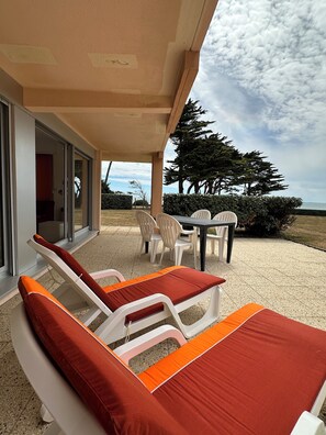 A covered outdoor seating area with lounge chairs and a table, overlooking a landscaped garden and a view of the sea. - Ground-floor apartment facing the sea with a large terrace (Pornic)