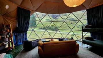 Een tent met uitzicht op een groen landschap, een bank, een boekenkast en een stapelbed.