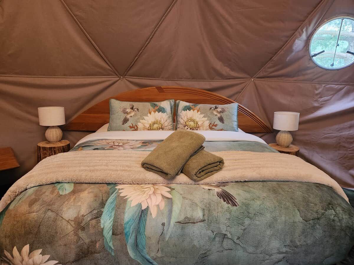 Ein Zelt-ähnliches Zimmer mit einem Bett, floralem Bettbezug, zwei Nachttischlampen und einem Fenster.