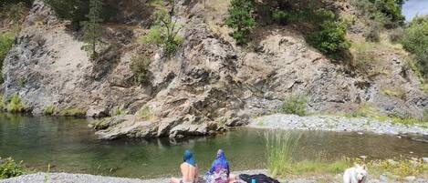 A rocky riverbank with a person and a dog, and a body of water in the background.