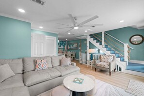 A living room with a sofa, chairs, a round table, a staircase with blue steps, and a ceiling fan. - Harbor Front Retreat~Fishing Dock~Minutes to the Private Beach~Water Taxi Location! (Destin)