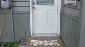 Una puerta blanca con un felpudo de 'welcome', un buzón y una caja de servicios a la izquierda.