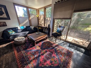 Ein Wohnzimmer mit einer Couch, einem Couchtisch, einem gemusterten Teppich und einem Sessel neben einem großen Fenster.