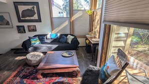 Un salón acogedor con sofá, reposapiés y mesa de centro, una alfombra y una ventana con persianas.