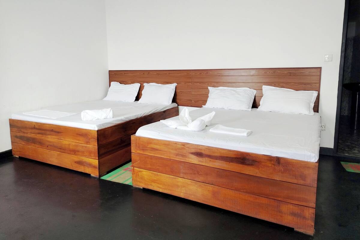 Una habitación de hotel con dos camas de madera, ropa blanca y un tapete con estampado rojo y verde.