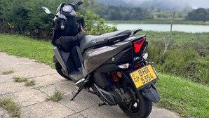 Una motocicleta estacionada en un camino pavimentado, con una vista panorámica de un lago y montañas al fondo.