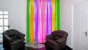 Una habitación con dos sillones de cuero, una mesa de vidrio y una cortina colorida.