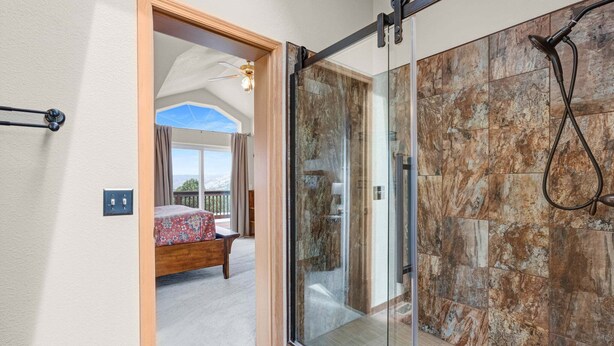 Un baño con cabina de ducha de vidrio, una cama con colcha estampada y vistas a un balcón.