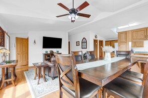 Ein Essbereich mit einem großen Holztisch, Stühlen, einem Deckenventilator und einer Küche im Hintergrund.