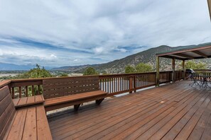 Eine Holzterrasse mit einer Bank und einem Tisch, mit Blick auf eine gebirgige Landschaft.