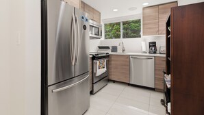 A modern kitchen with stainless steel appliances, wooden cabinets, a dishwasher, and a window with a view of greenery. - 3BR Dunbar Family Retreat Near UBC/Transit (Vancouver)