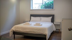 A neatly made bed with white linens and two towels, a bedside table, a nightstand, and a window with a view of greenery. - 3BR Dunbar Family Retreat Near UBC/Transit (Vancouver)