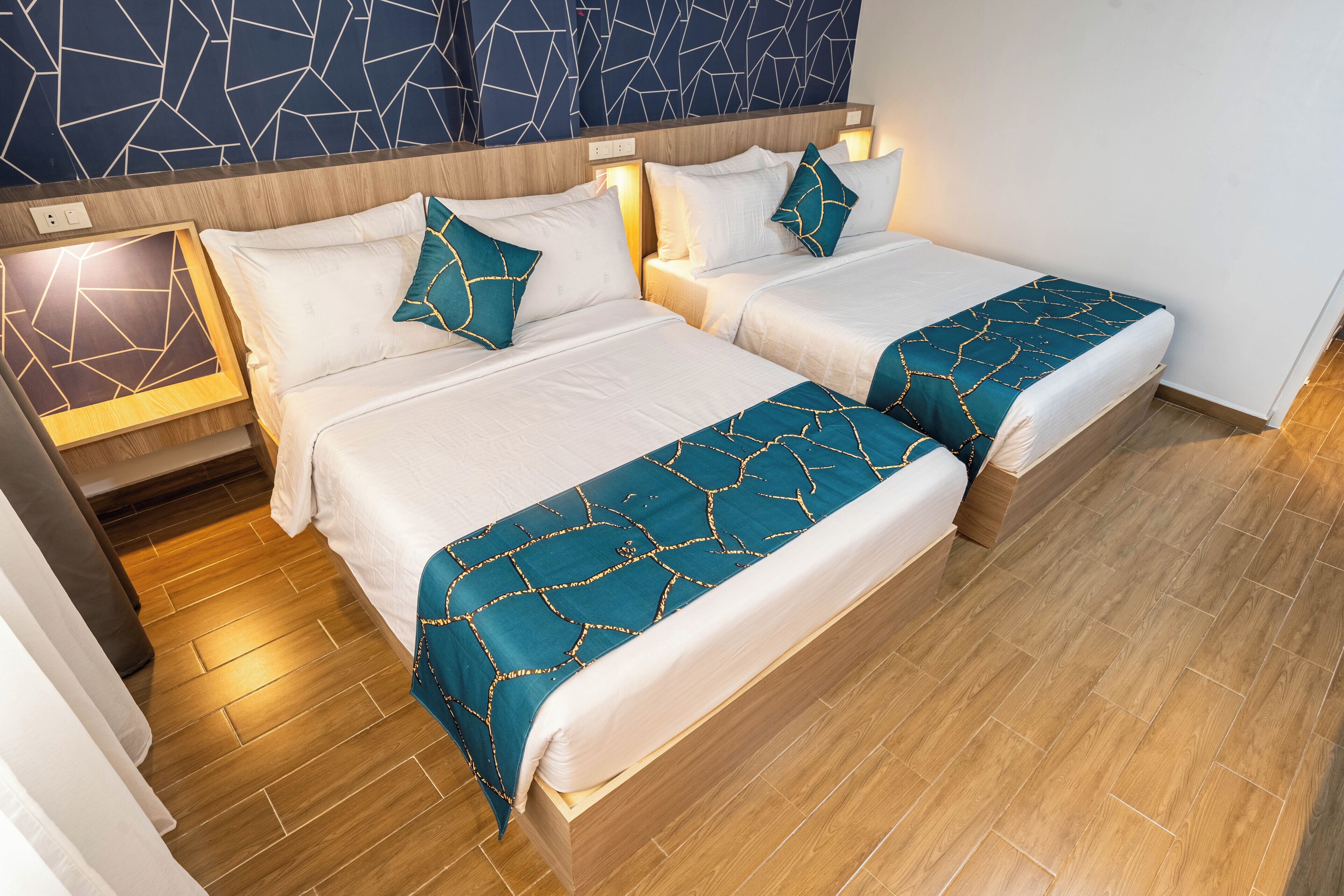 Habitación de hotel con dos camas, suelo de madera y pared con diseño geométrico.
