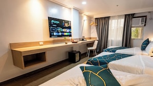 Habitación de hotel con televisión, escritorio, dos camas, una silla y ventana con cortinas.