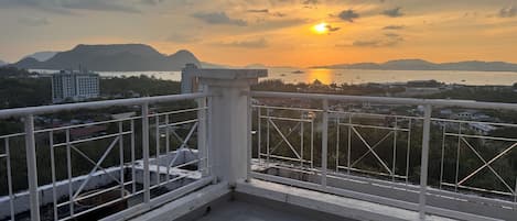 A balcony with a metal railing overlooking a cityscape and a sunset.