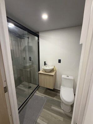 A modern bathroom with a glass shower enclosure, a sink with a mirror, and a toilet. - Tranquil 1-bedroom hotel suites with AC in Gro,
2 pools and Jacuzzy (Gro.)