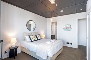 A hotel room with a bed, bedside lamps, a mirror, a wall sign, and a door.