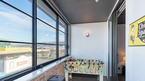 Une pièce avec un baby-foot sur lequel est écrit « FOOTBALL », une fenêtre donnant sur des immeubles et un luminaire fixé au mur.