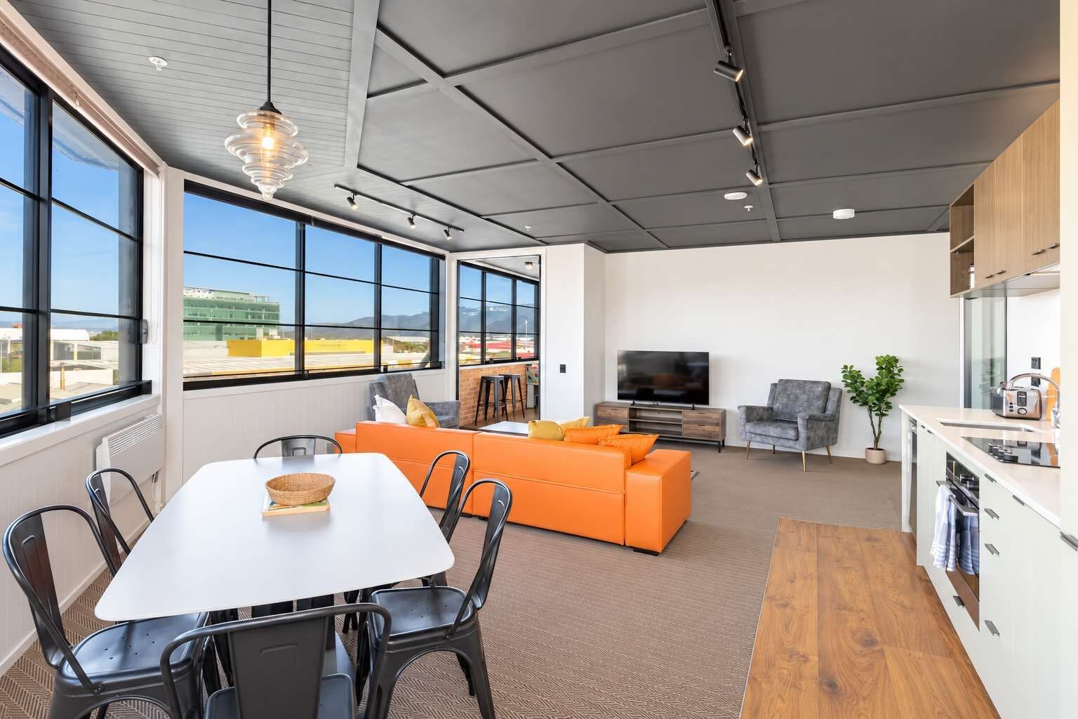 A modern living room with a dining area, large windows, and a kitchen.