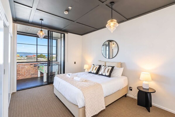 A hotel room with a bed, bedside lamps, a mirror, and a view of a soccer table through a glass door.