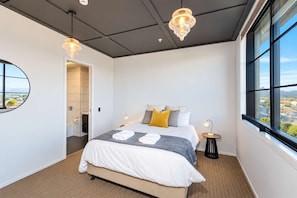 Une chambre d’hôtel moderne avec un grand lit, une vue par la fenêtre et un miroir rond accroché au mur.