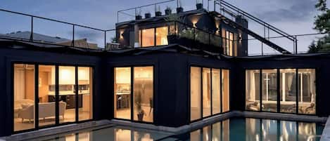 A modern house with a pool, large glass doors, and a balcony with plants.