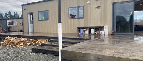A building with a large garage door, a wooden deck, and a gravel area with a pile of wood.