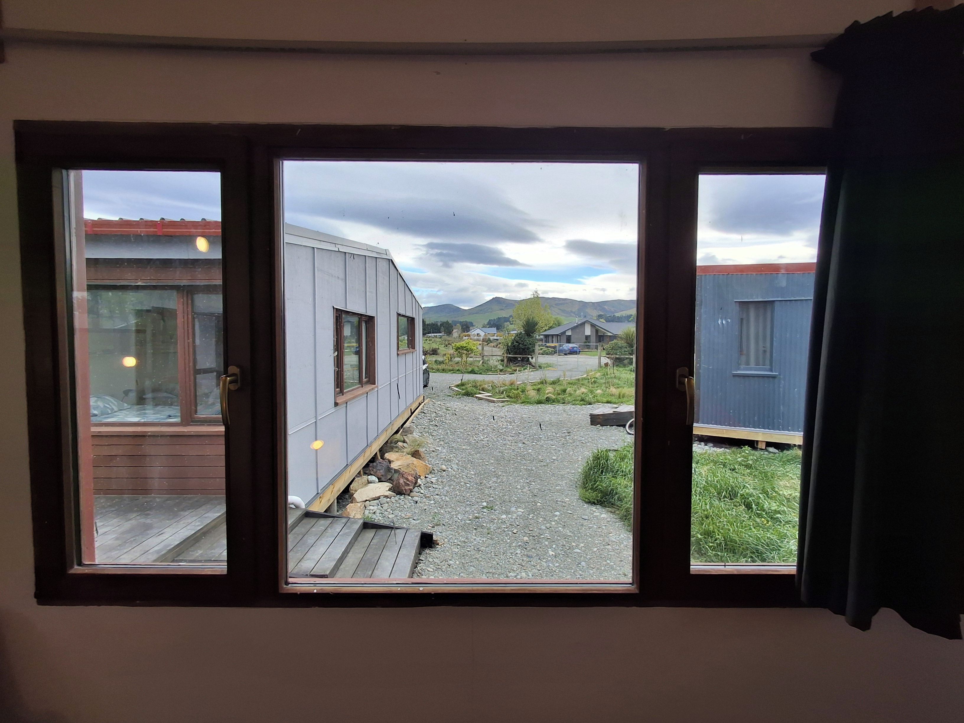 A room with a large sliding glass door leading to an outdoor area with a gravel path, wooden deck, and a view of a residential area with houses and mountains.