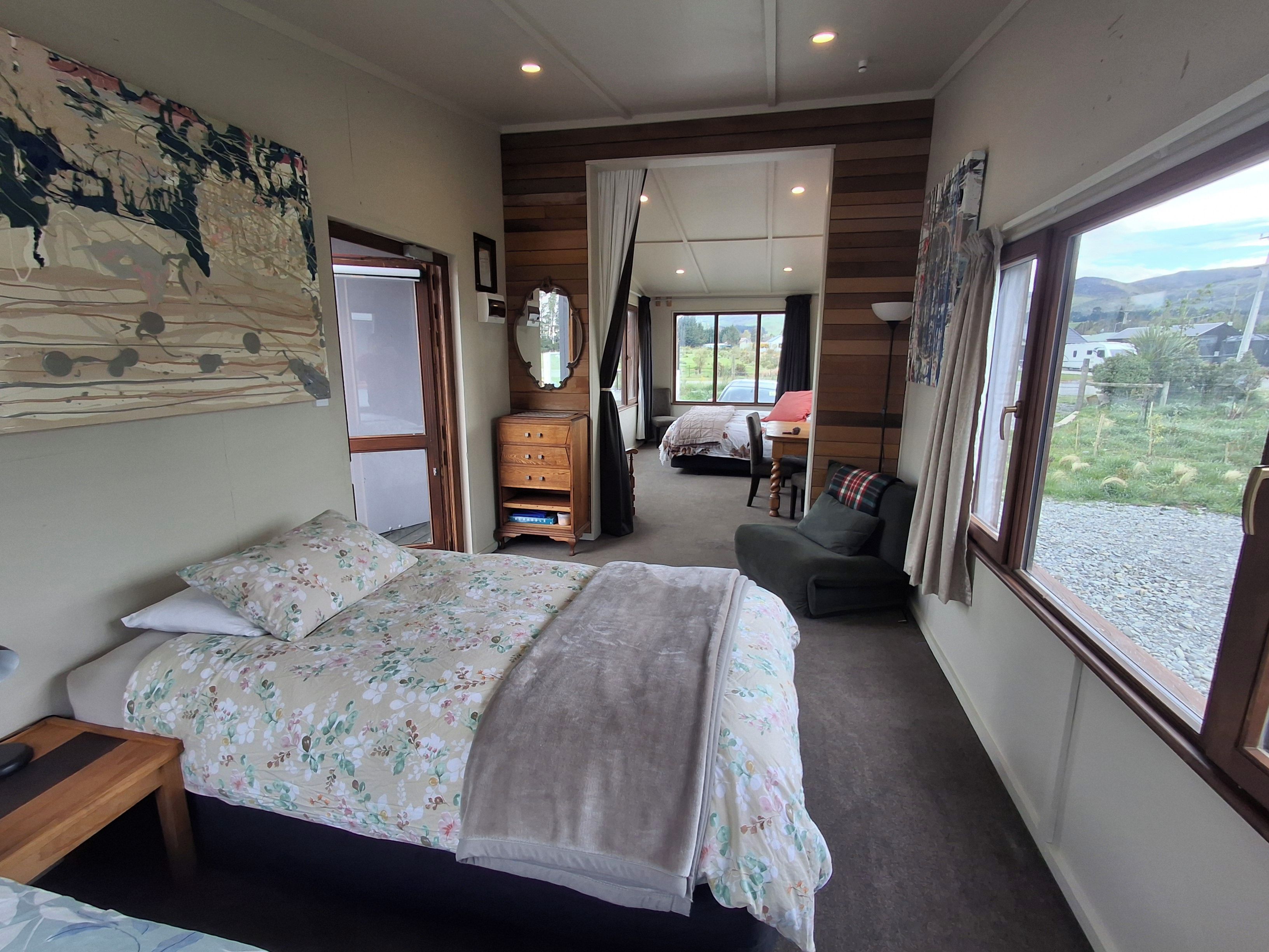 A bedroom with a bed, a dresser, a desk, and a view of the outdoors.