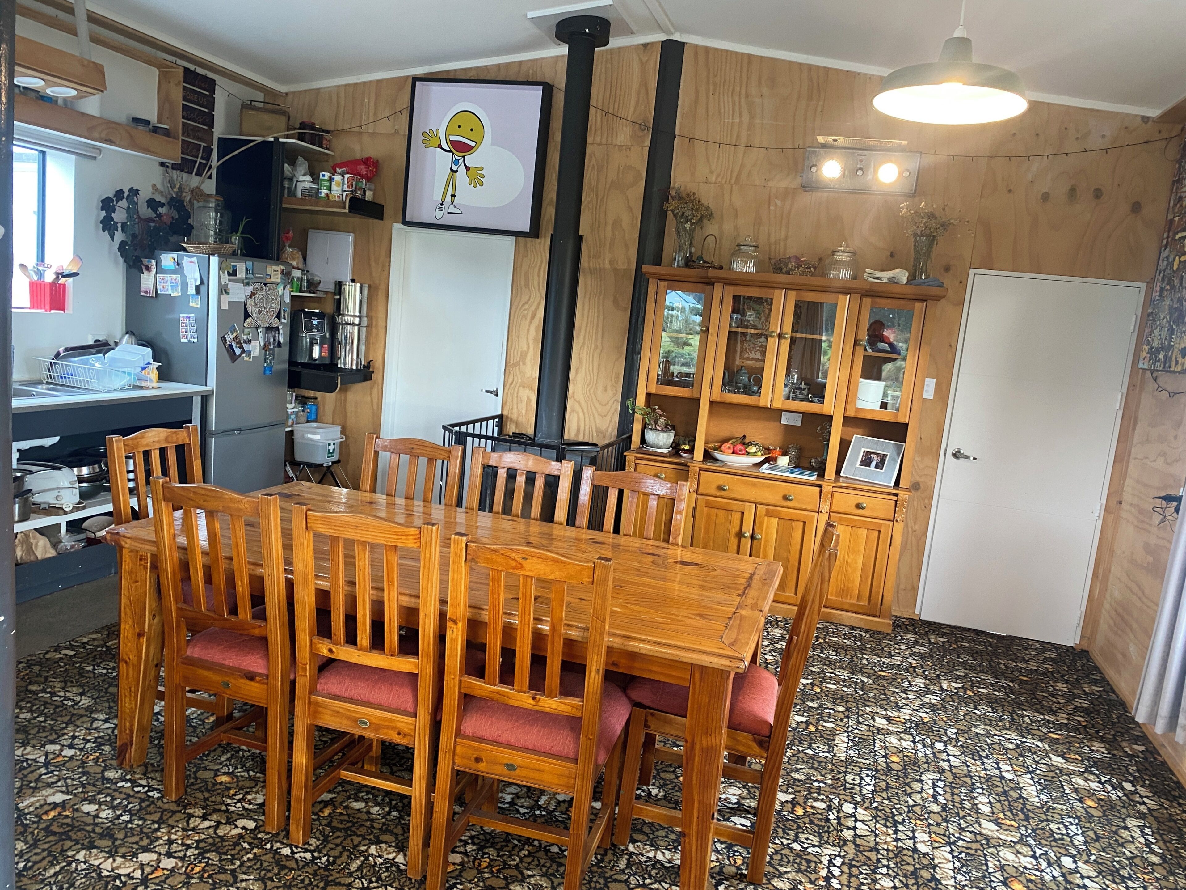 Een eethoek met een houten tafel en stoelen, een keuken met een koelkast en planken, en een kast met glazen deuren.