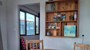 Ein Essbereich mit einem Holztisch und Stühlen, einem Bücherregal mit diversen Gegenständen und einem Fenster mit Blick.