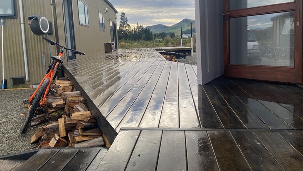 A modern building with a wooden deck, a bike, and a pile of firewood. - Rural Retreat: Group Bookings, Family Adventures & Work Trips (Lumsden)