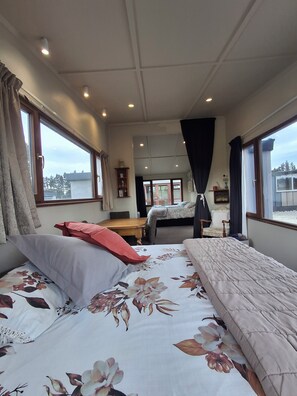 Un dormitorio con una cama grande, una cama más pequeña, una silla, una mesa y un ventanal con cortinas.