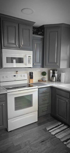A kitchen with grey cabinets, a white microwave, a stove, and a coffee maker. - Midtown Oasis 
3 Bedrooms house in  Rogers with  AC, private pool and more (Rogers)